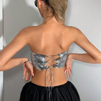 Person wearing a silver sequin top with thin straps against a plain background