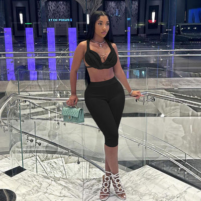 A model wearing a black halter bikini top with lace-up details and backless design, paired with figure-hugging cropped pants.