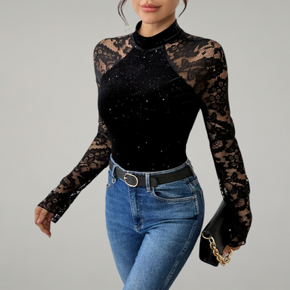 Woman wearing a black long-sleeve top with lace details and blue jeans on a gray background