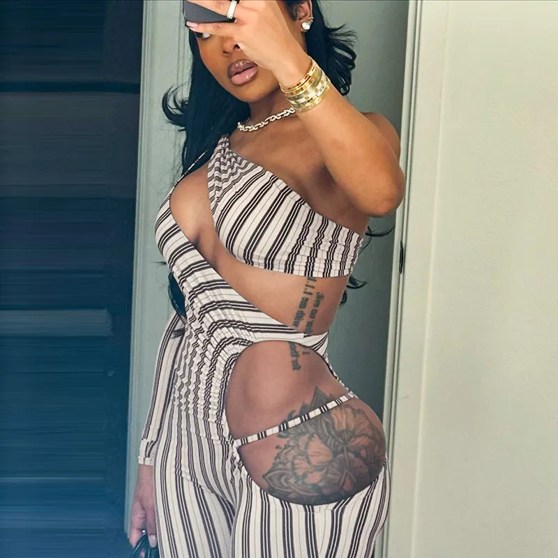 A woman wearing a striped slim-fit jumpsuit with hollow-out details. The jumpsuit is primarily monochrome with a bold striped pattern.