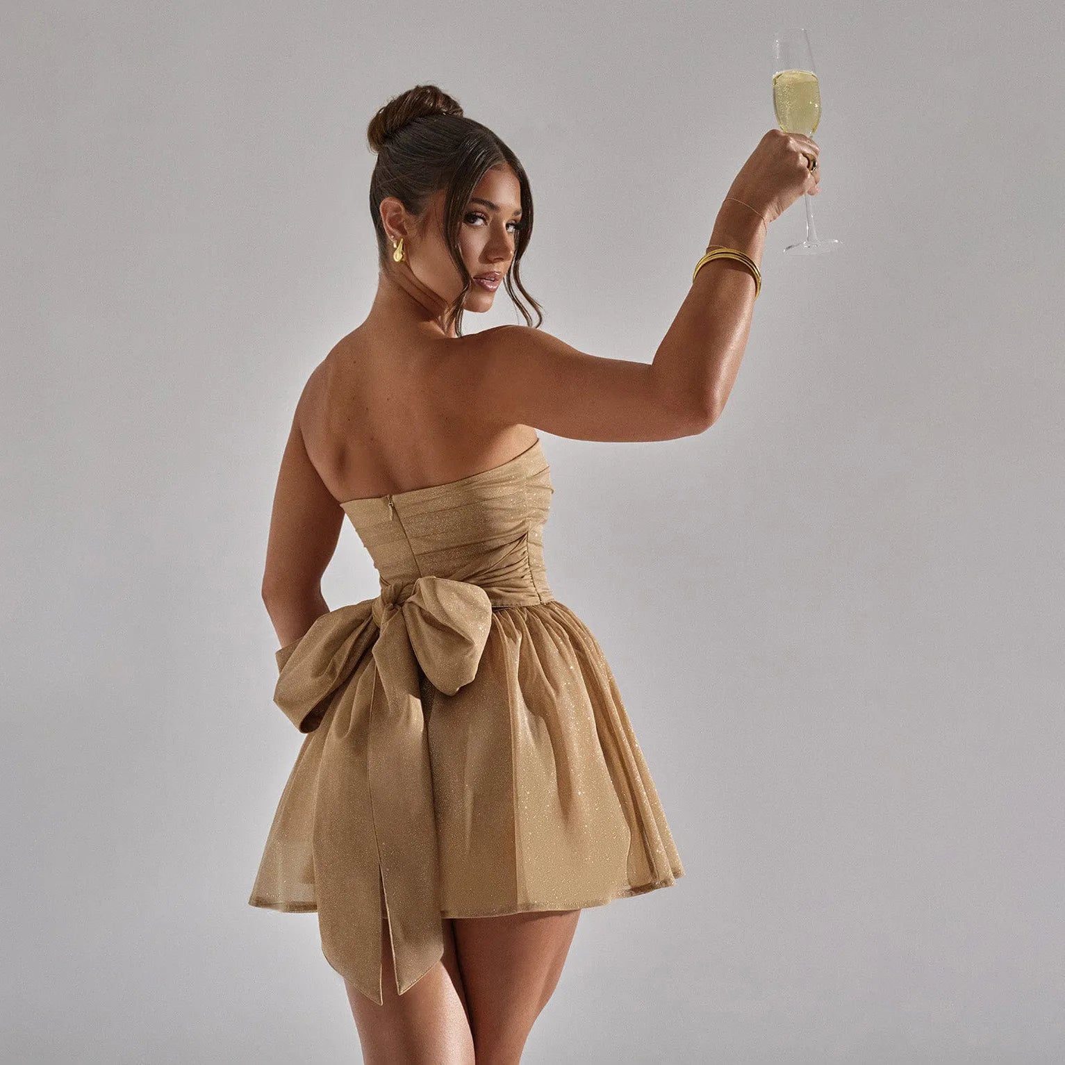 Woman in a beige dress holding a glass of champagne against a gray background