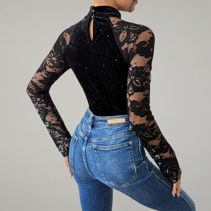 Person wearing a black lace long-sleeve top and blue jeans on a gray background