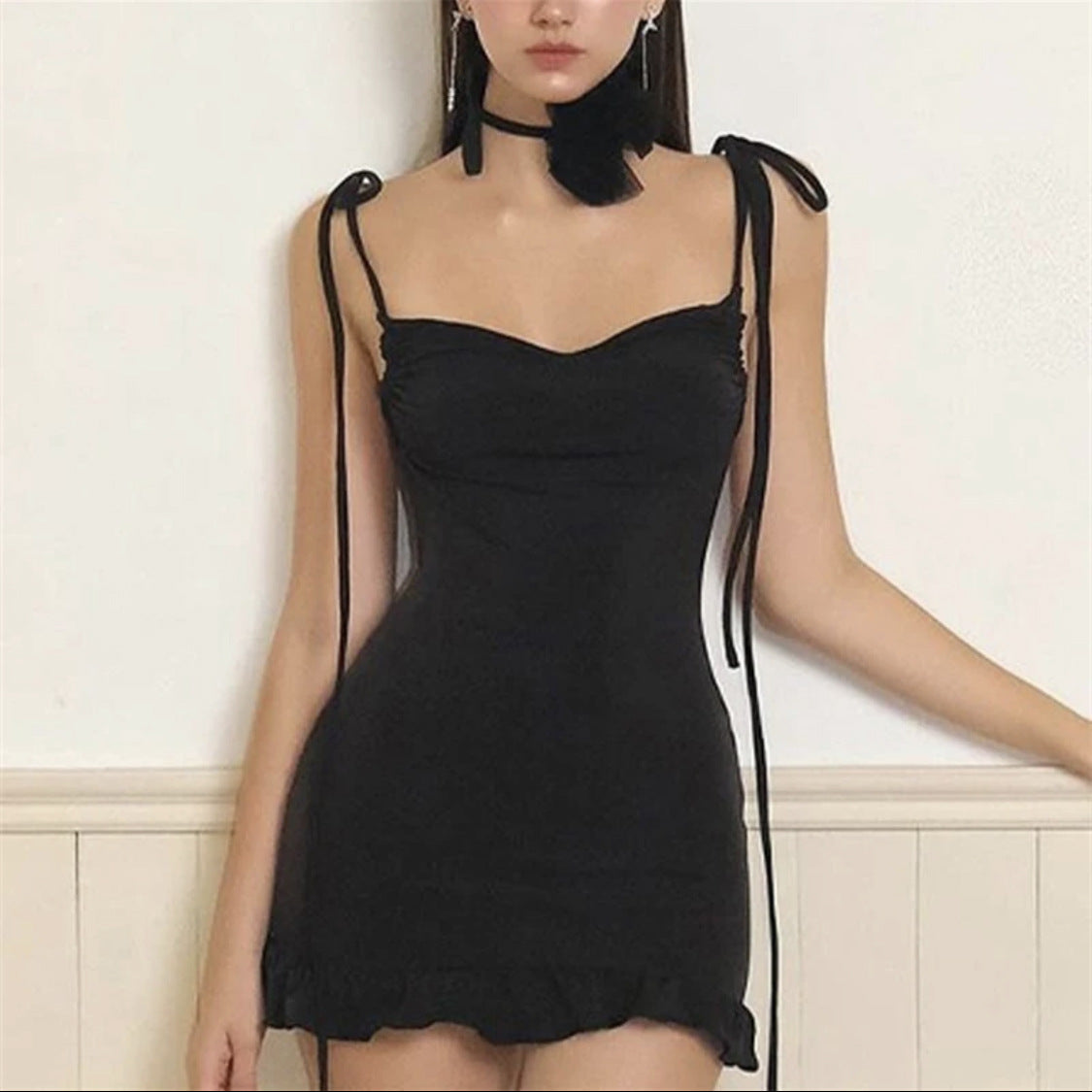 Black dress with tie straps worn by a model against a white background