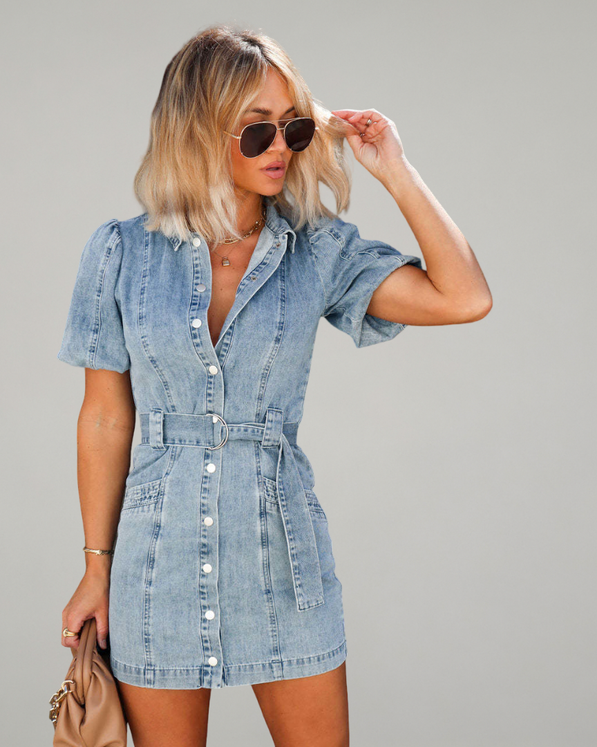 Woman wearing a denim dress with sunglasses on a gray background
