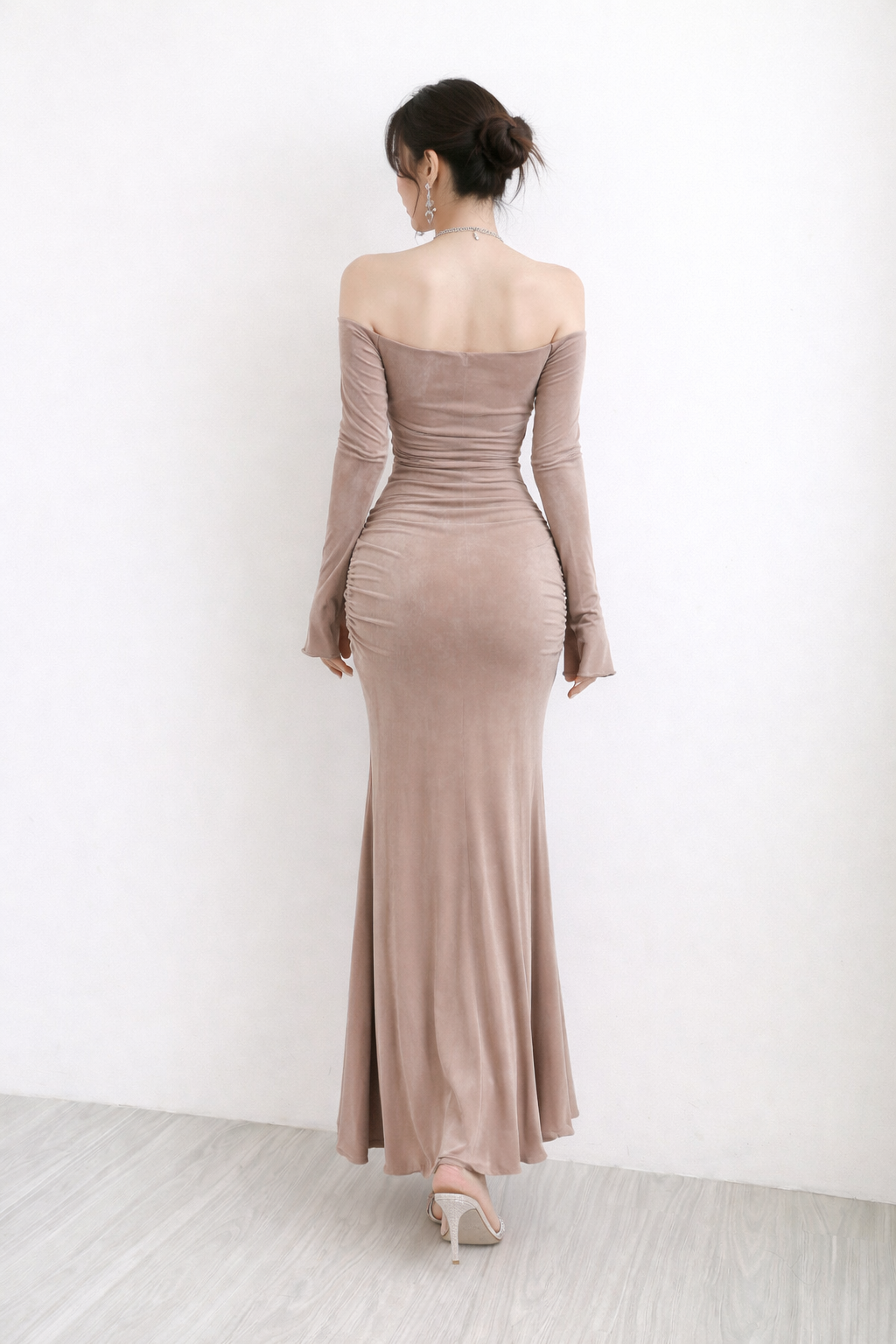 Woman wearing a long, off-shoulder dress with long sleeves against a white background