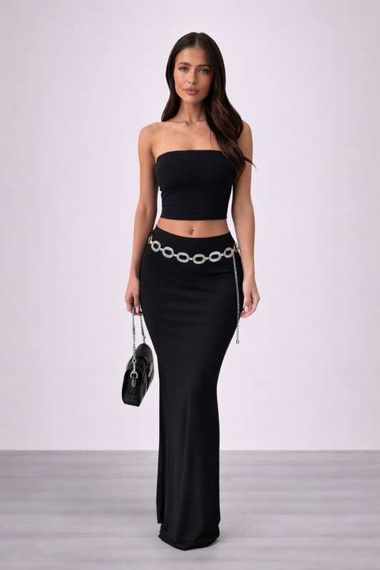Woman wearing a black strapless top and black skirt with a chain detail on a white background