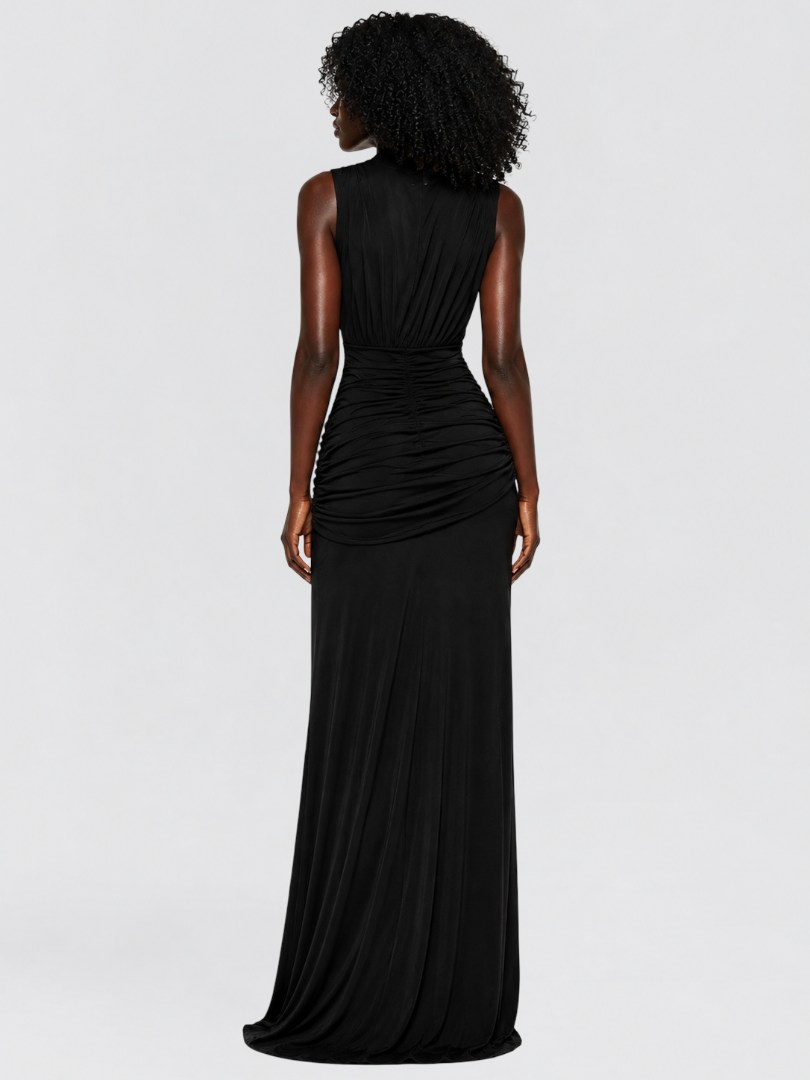 A woman shown from the back wearing a sleeveless black maxi dress with ruched draping at the waist, photographed against a light gray studio background.