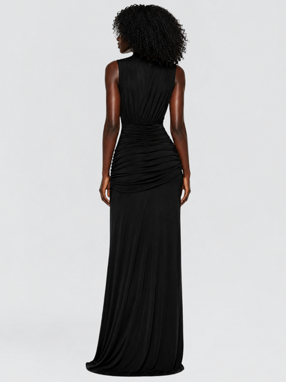 A woman shown from the back wearing a sleeveless black maxi dress with ruched draping at the waist, photographed against a light gray studio background.