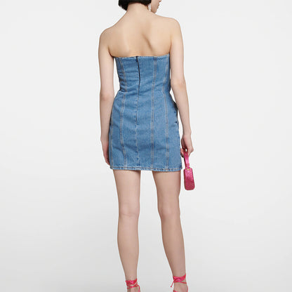 Woman wearing a strapless denim dress holding a pink handbag on a white background